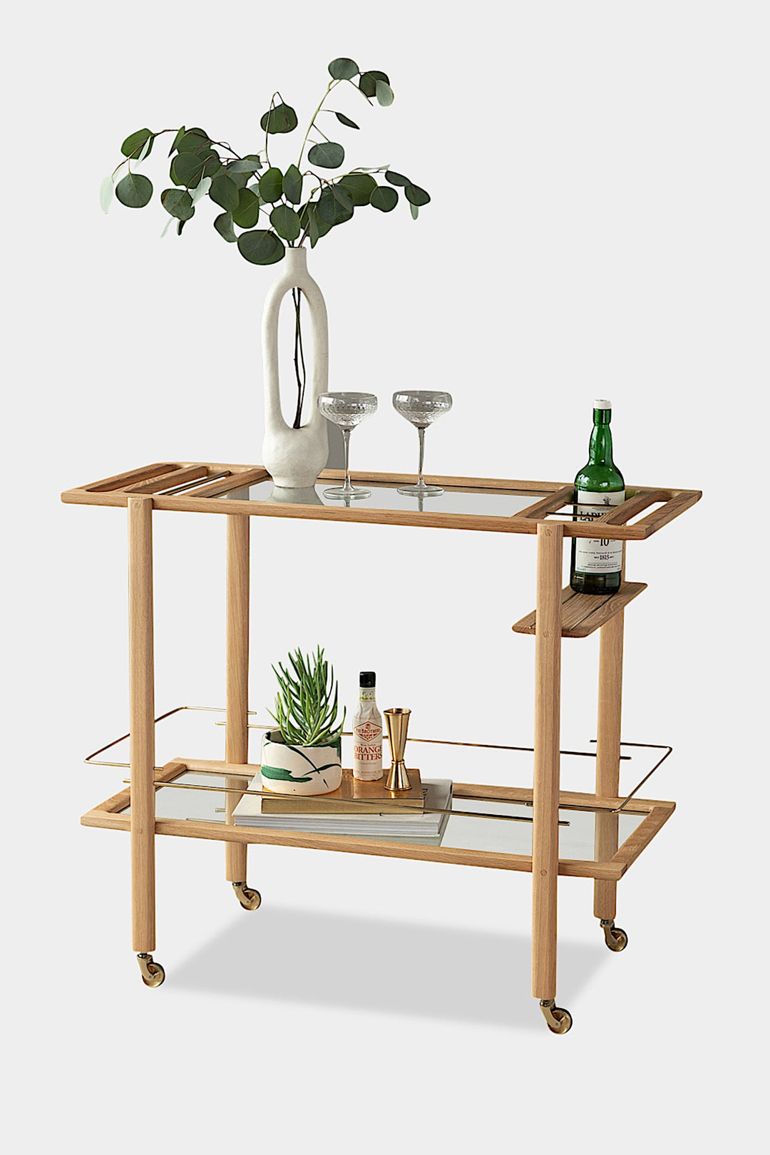 The BAR Cart from Earl Home is a solid wood bar cart on wheels with exquisite hand-cut joinery, featuring two shelves: a robust wood top and an elegant lower shelf made of tempered glass panels.