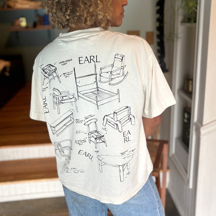 Person wearing a t-shirt with 'Earl' and furniture illustrations on the back, standing in a room.