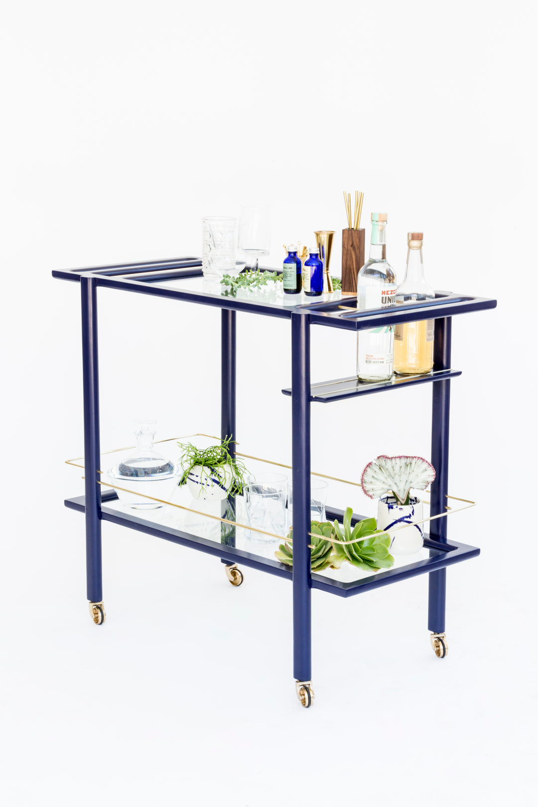 The BAR Cart from Earl Home is a solid wood bar cart on wheels with exquisite hand-cut joinery, featuring two shelves: a robust wood top and an elegant lower shelf made of tempered glass panels.