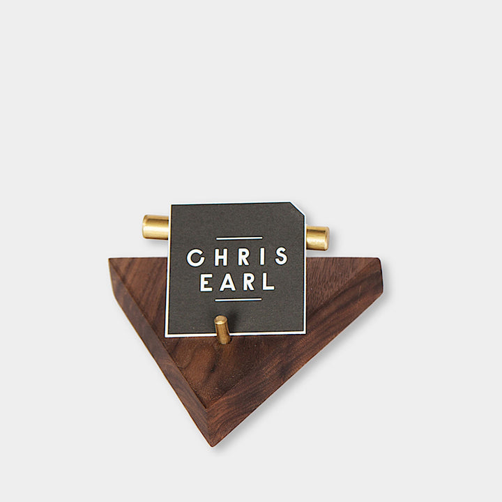 The BUSINESS Card Holder, expertly crafted by Earl Home from wood and brass, showcases a card with "CHRIS EARL." This elegant accessory can be customized to perfectly fit any desk or office setting.