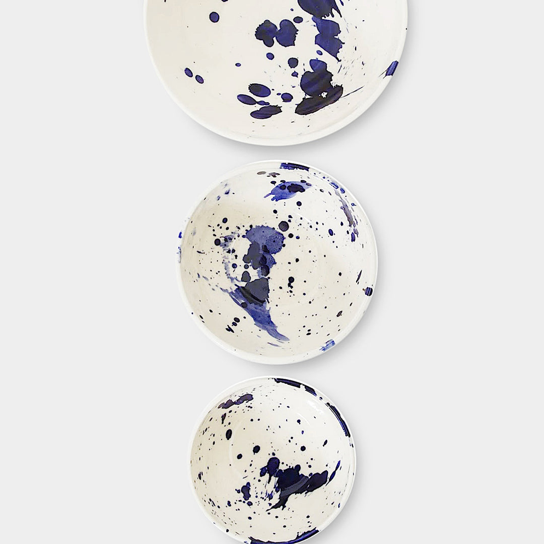 Earl Home's NESTING Bowls set includes three hand-thrown ceramic pieces with a blue splatter pattern on a plain background. Dishwasher and microwave safe, they blend artisanal design with daily functionality.