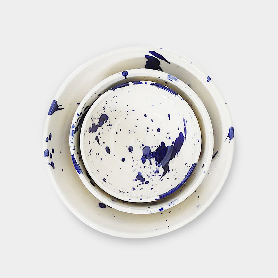 Earl Home's NESTING Bowls set includes three hand-thrown ceramic pieces with a blue splatter pattern on a plain background. Dishwasher and microwave safe, they blend artisanal design with daily functionality.