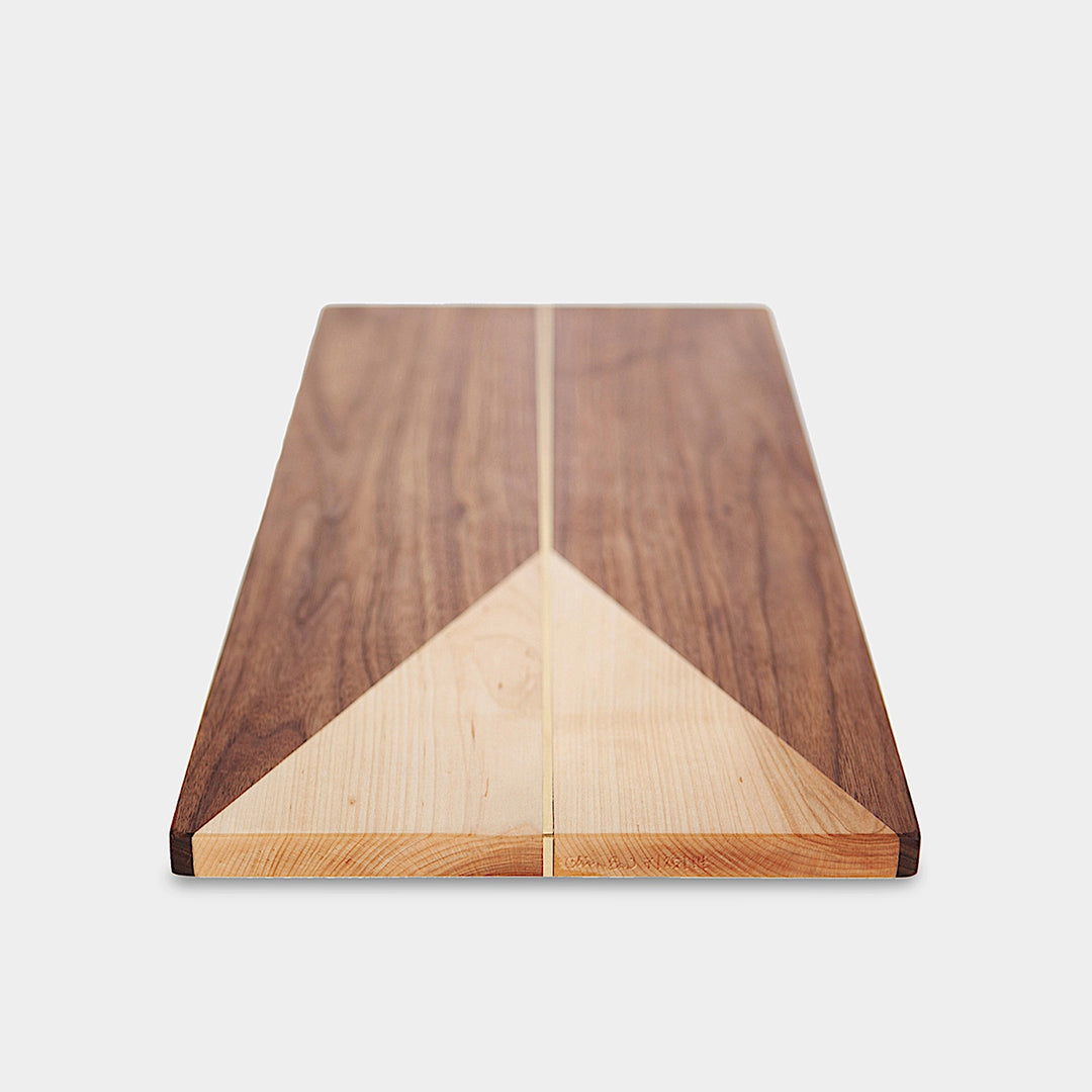 The RECTANGLE Cheese Board by Earl Home is a handcrafted serving board featuring a natural wood grain and accented with an off-center pale triangle on the left, ideal for elegant entertaining.