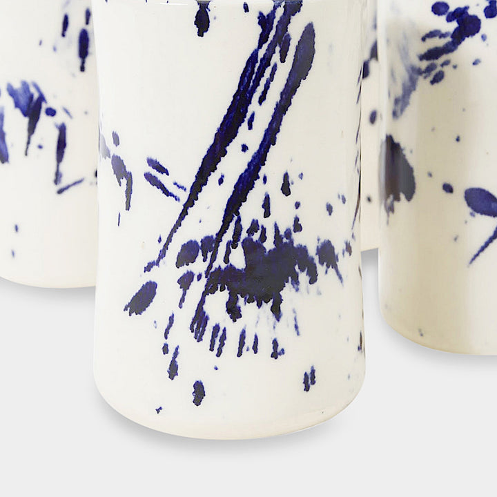 Earl Home's TUMBLR set includes four white ceramic cups with captivating blue brush stroke splatter designs that showcase their hand-thrown artistry.