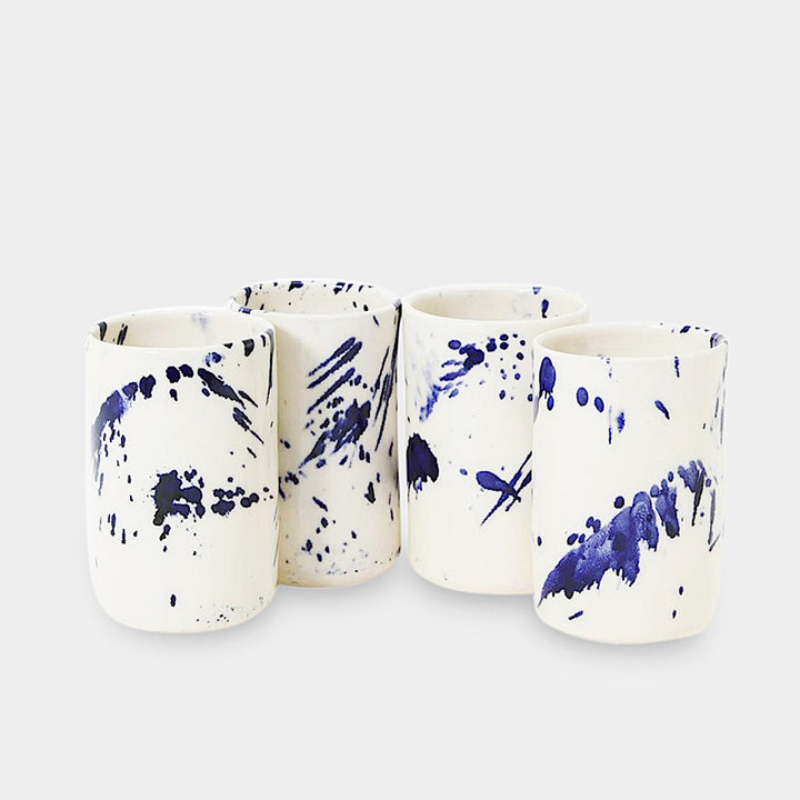 Earl Home's TUMBLR set includes four white ceramic cups with captivating blue brush stroke splatter designs that showcase their hand-thrown artistry.