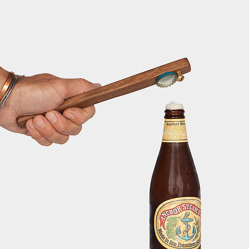 A bottle of Anchor Steam beer is topped with an Earl Home WOOD + BRASS Bottle Opener, combining style and practicality.