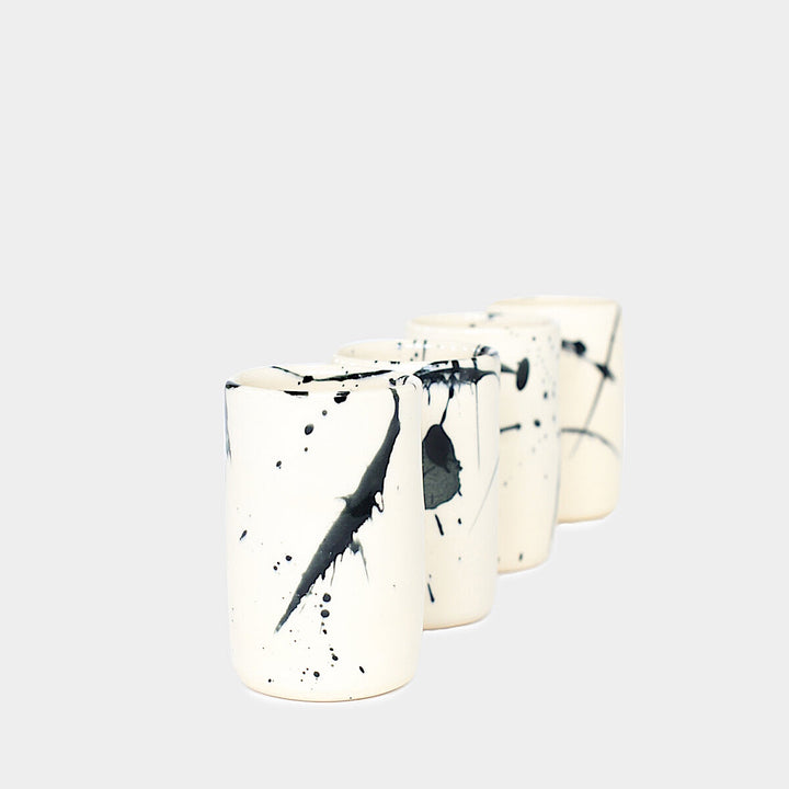 Earl Home's TUMBLR set includes four white ceramic cups with captivating blue brush stroke splatter designs that showcase their hand-thrown artistry.