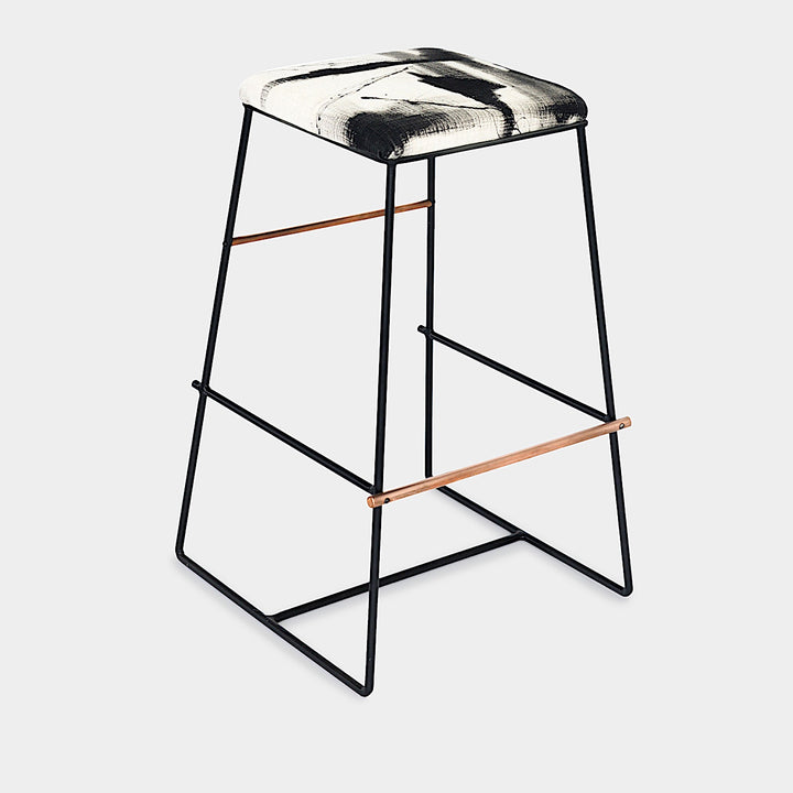 The METAL Counter Stool by Earl Home boasts sleek black metal legs and a square seat upholstered in a bold black and white abstract pattern, with customizable finishes.