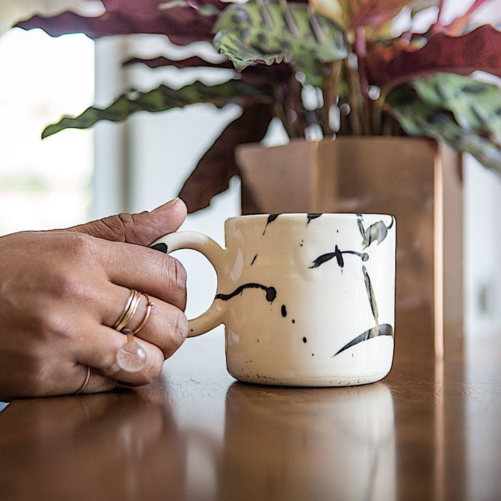 Earl Home's CIRCLE Mug is a hand-thrown white ceramic mug with black brush stroke splatters and a round handle.