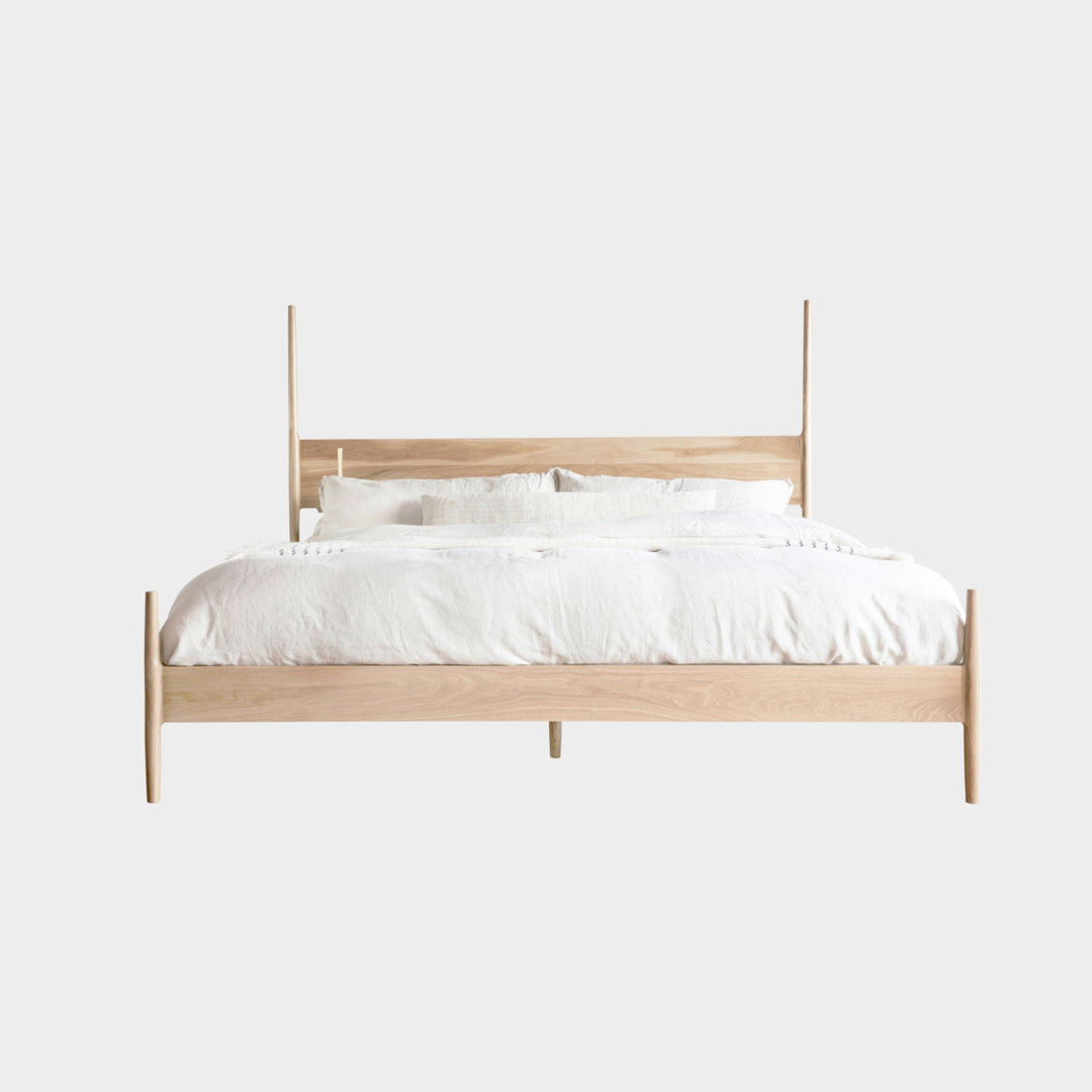 The DANSK Bed by Earl Home features a solid wood frame with a tall headboard and luxurious white bedding, creating your perfect sanctuary. Crafted in walnut, it exemplifies quality and is handmade to order.