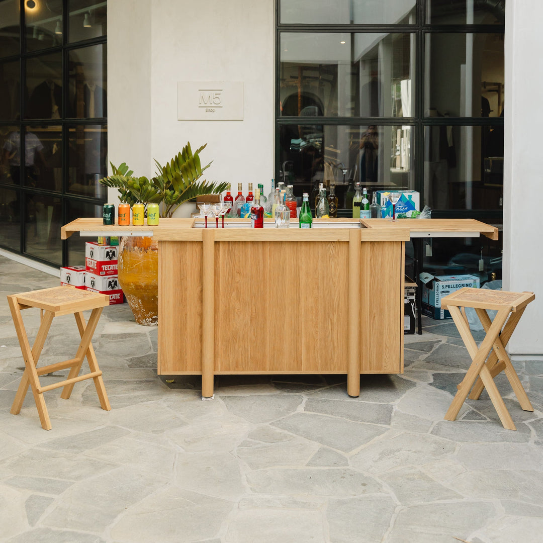 The LAPILO Folding Stool by Earl Home features an angular solid wood frame with a marbled cork seat and cross-legged design in a sleek finish.