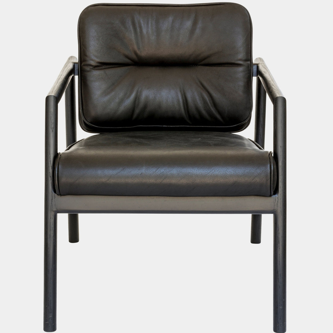 The MORESBY Lounge Chair by Earl Home is a modern, handmade piece featuring a sleek dark frame and a custom upholstered black leather cushion.