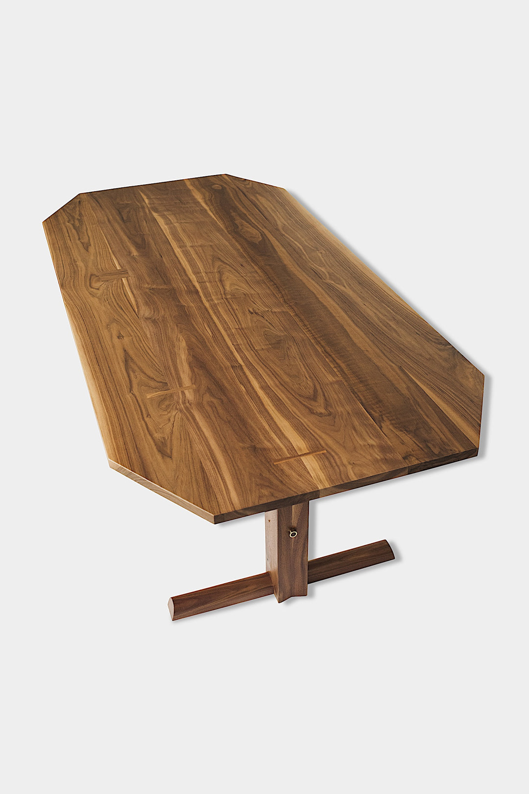 The BRIG Dining Table by Earl Home is a handmade piece featuring a rectangular solid wood top with angled corners, supported by two sturdy pedestal legs connected by a trestle base.