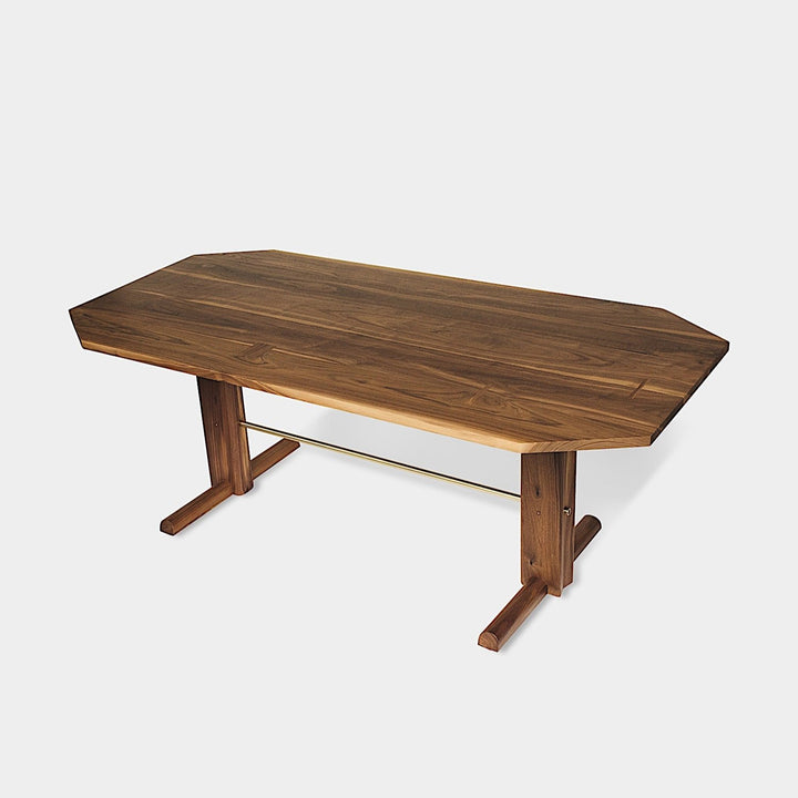 The BRIG Dining Table by Earl Home is a handmade piece featuring a rectangular solid wood top with angled corners, supported by two sturdy pedestal legs connected by a trestle base.