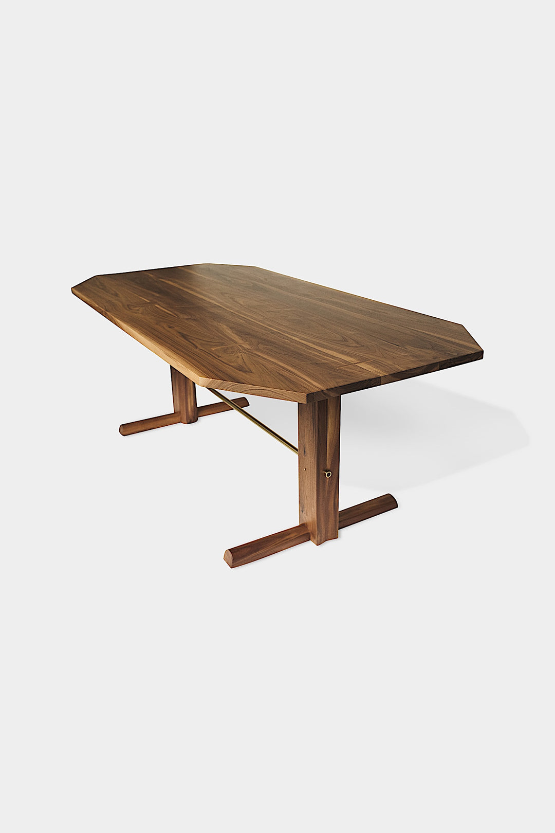 The BRIG Dining Table by Earl Home is a handmade piece featuring a rectangular solid wood top with angled corners, supported by two sturdy pedestal legs connected by a trestle base.