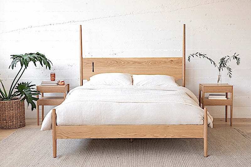 The DANSK Bed by Earl Home features a solid wood frame with a tall headboard and luxurious white bedding, creating your perfect sanctuary. Crafted in walnut, it exemplifies quality and is handmade to order.