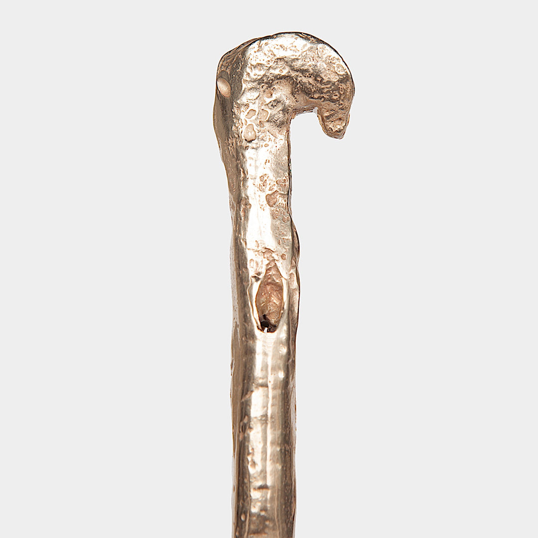 Close-up of the weathered, metallic handle of a CASSOWARY 4-Way Bar Tool by Earl Home, crafted from solid brass with a textured surface and resembling an elegant walking cane, against a plain background.