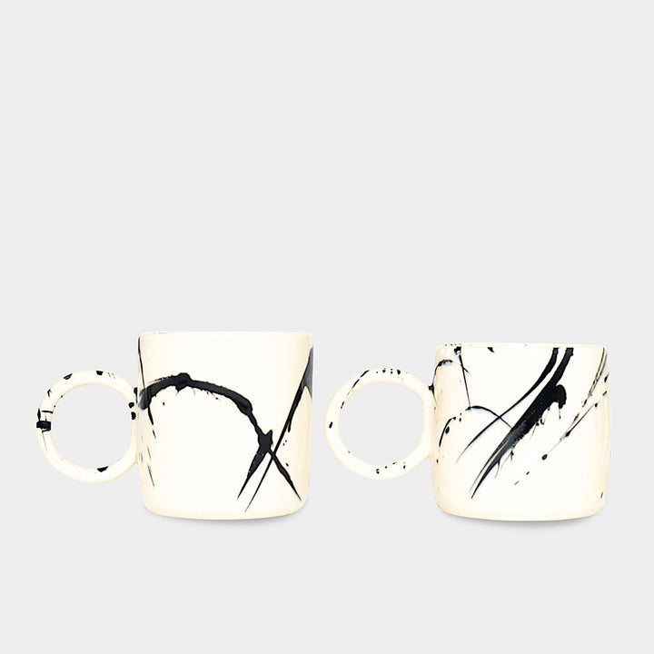 Earl Home's CIRCLE Mug is a hand-thrown white ceramic mug with black brush stroke splatters and a round handle.