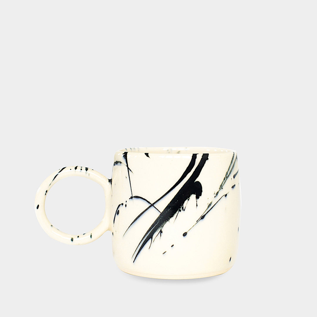 Earl Home's CIRCLE Mug is a hand-thrown white ceramic mug with black brush stroke splatters and a round handle.