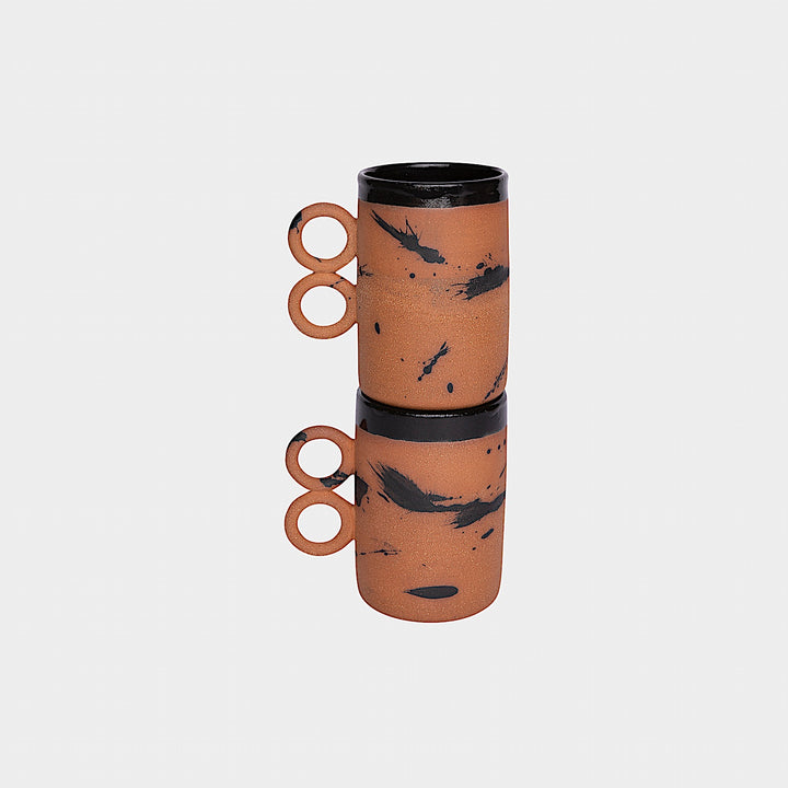 The Earl Home DOUBLE Handle Mug set includes two brown ceramic mugs, each featuring a unique round handle and white abstract patterns. Hand-thrown for artisanal charm, these mugs are perfect for those who appreciate the delicate artistry of ceramic craftsmanship.