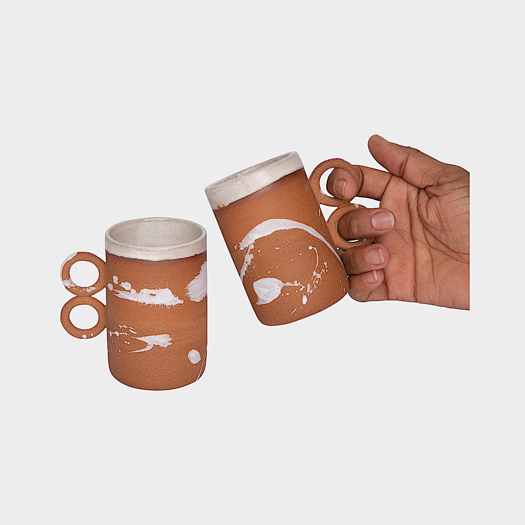 The Earl Home DOUBLE Handle Mug set includes two brown ceramic mugs, each featuring a unique round handle and white abstract patterns. Hand-thrown for artisanal charm, these mugs are perfect for those who appreciate the delicate artistry of ceramic craftsmanship.