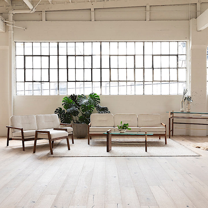 A lifestyle living room scene of the MORESBY Love Seat by Earl Home, showcasing a walnut solid wood constructed frame and maharam plume ciabatta ivory linen  upholstered cushions.