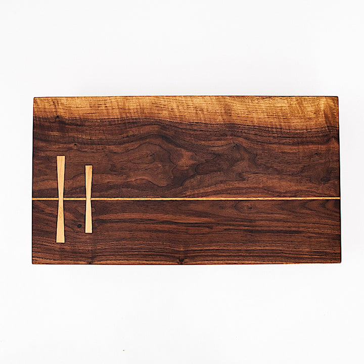 The Rectangle Cutting Board by Earl Home is a wooden board featuring a natural oak grain pattern with two parallel walnut inlays near one end.