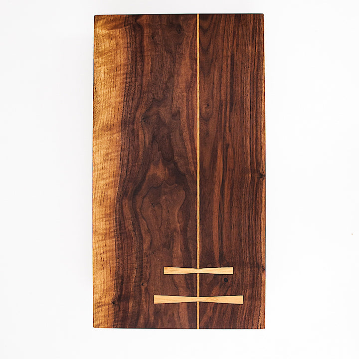 The Rectangle Cutting Board by Earl Home is a wooden board featuring a natural oak grain pattern with two parallel walnut inlays near one end.