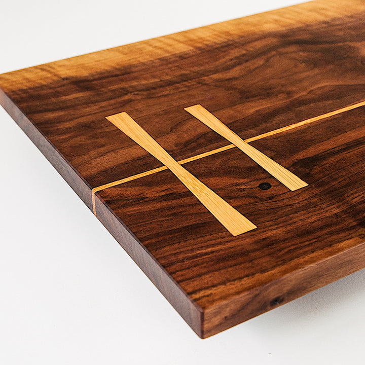 The Rectangle Cutting Board by Earl Home is a wooden board featuring a natural oak grain pattern with two parallel walnut inlays near one end.