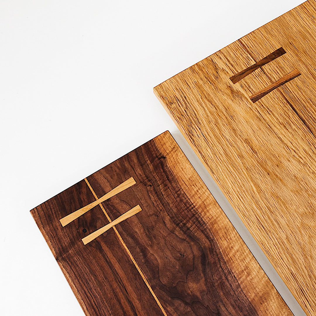 The Rectangle Cutting Board by Earl Home is a wooden board featuring a natural oak grain pattern with two parallel walnut inlays near one end.