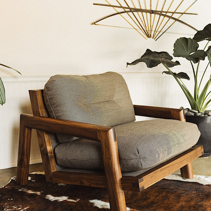 The Earl Home Walnut TAMBU Lounge Chair boasts olive leather upholstery, a sturdy walnut frame, and cushioned seat and backrest.