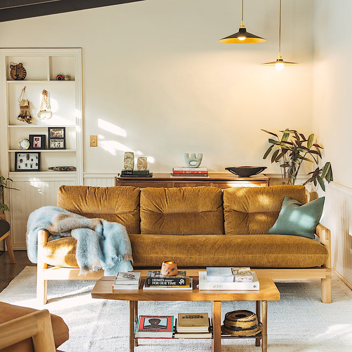 The White Oak TAMBU Sofa by Earl Home is a modern classic with a minimalist wooden frame of elegant White Oak, enhanced by three mustard cushions set against a white backdrop.