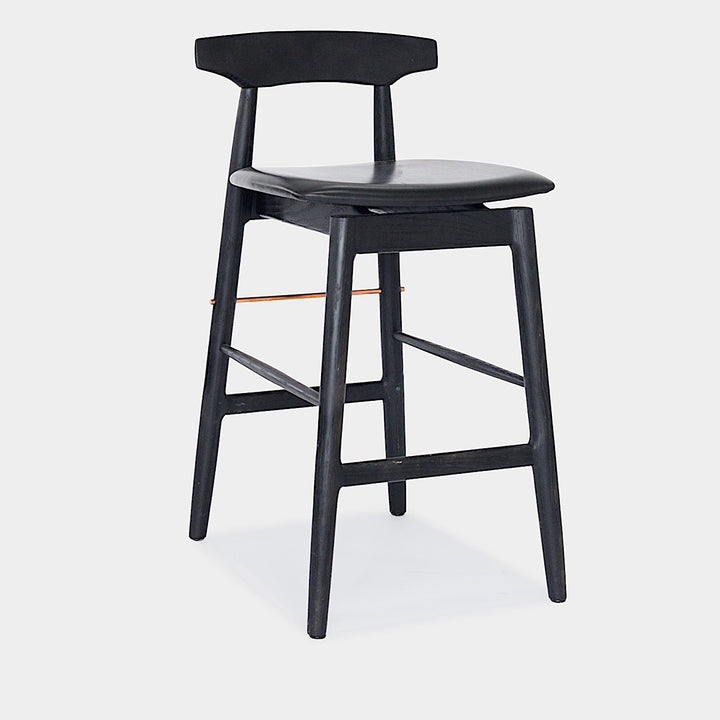 The WOOD High Stool (Bar Height) by Earl Home is a handcrafted wooden bar stool with a light finish, backrest, footrest, and simple design. It offers customizable upholstery to match any decor.