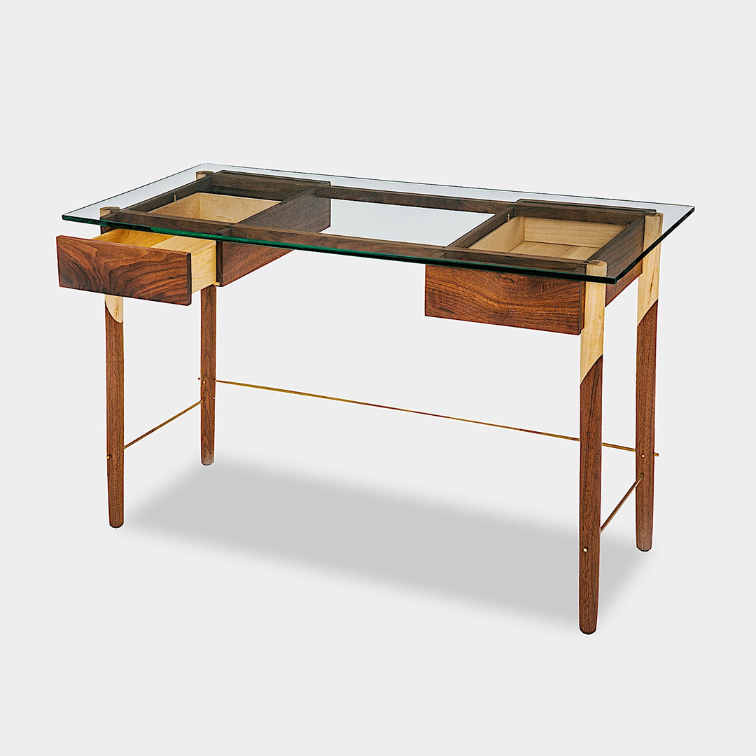 The WRITING Desk by Earl Home is an elegant glass desk with walnut and maple spliced wooden legs and a tempered glass top, Accompanied by a matching wooden chair. You can customize it to create your perfect workspace.