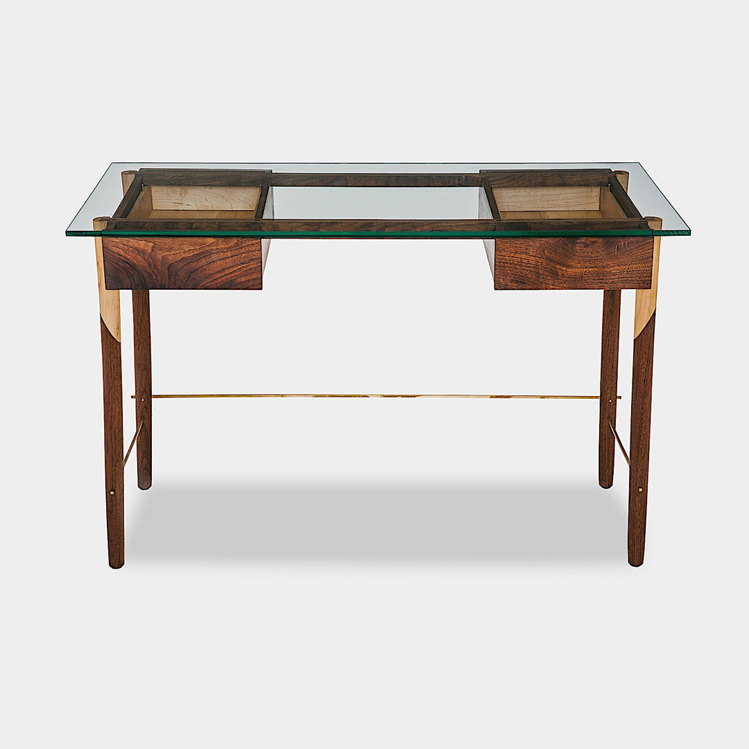 The WRITING Desk by Earl Home is an elegant glass desk with walnut and maple spliced wooden legs and a tempered glass top, Accompanied by a matching wooden chair. You can customize it to create your perfect workspace.