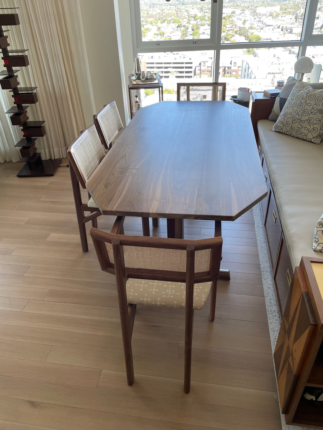 The BRIG Dining Table by Earl Home is a handmade piece featuring a rectangular solid wood top with angled corners, supported by two sturdy pedestal legs connected by a trestle base.