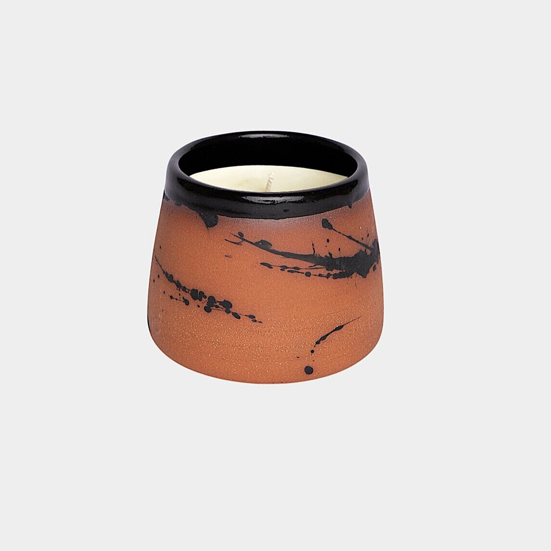 The Earl Home CANDLE is a white ceramic votive with a black splatter pattern, featuring an unlit cardamom-scented candle, set against a gray background.