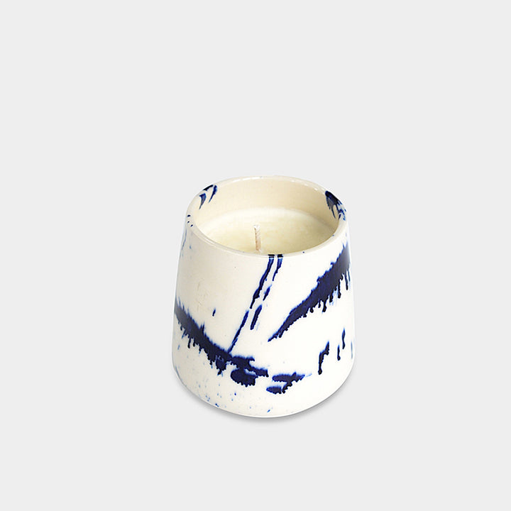 The Earl Home CANDLE is a white ceramic votive with a black splatter pattern, featuring an unlit cardamom-scented candle, set against a gray background.