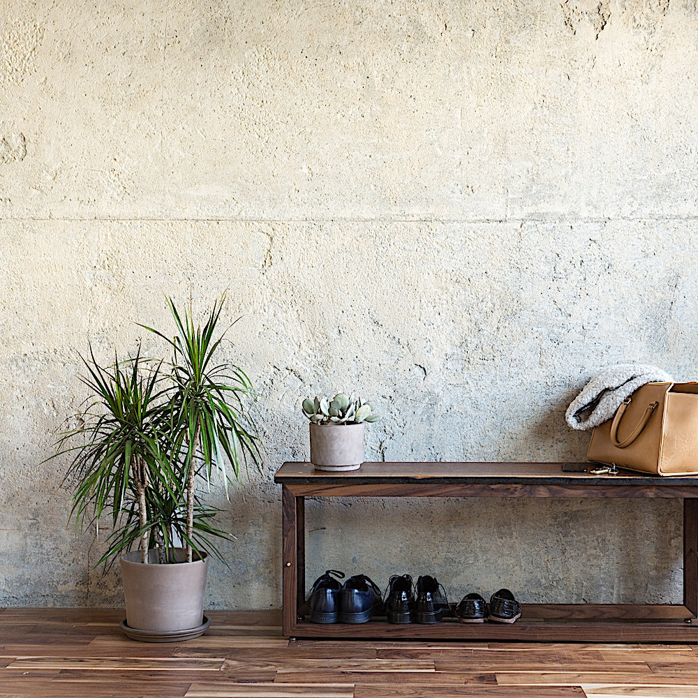 The Earl Home Walnut HAROLD Bench is a handcrafted masterpiece with a simple rectangular design and an open frame, featuring elegant walnut wood and brass detailing.