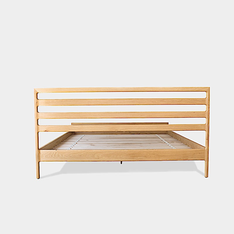 The LAMEL Bed by Earl Home is a hand-crafted bed frame with solid wood construction and a slatted headboard. It pairs beautifully with white pillows and a striped duvet, offering style and comfort. Available in custom bed sizes to fit your space perfectly.