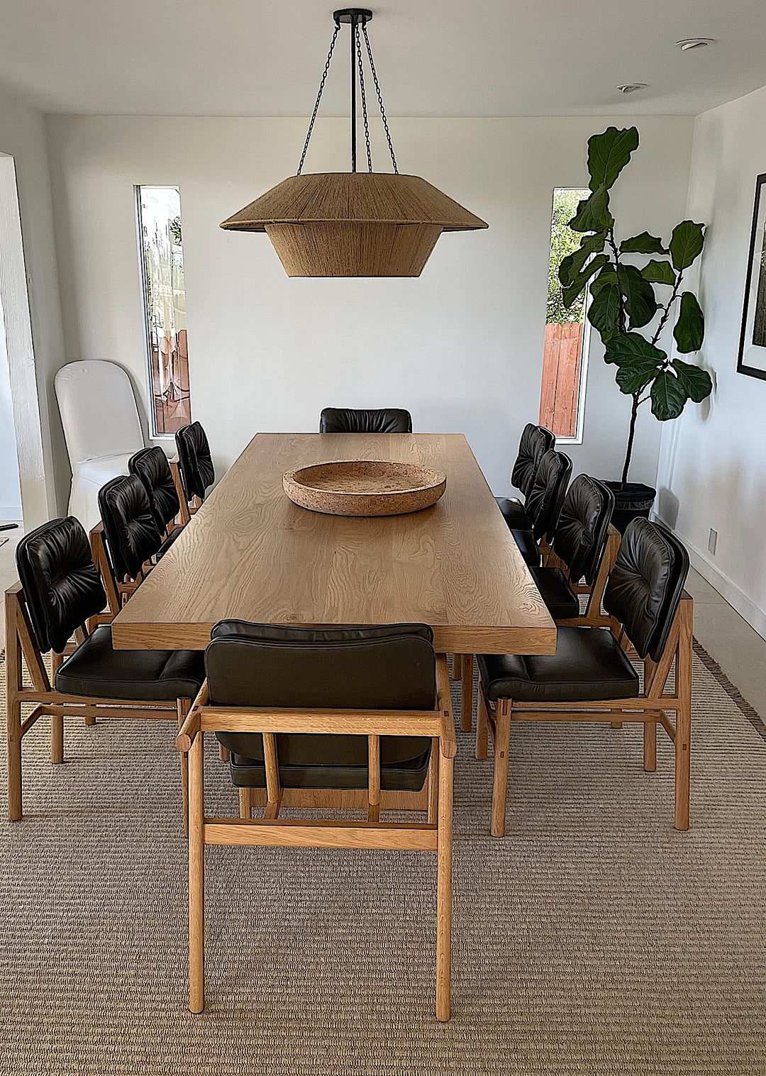 The MORESBY Dining Chair by Earl Home features a custom upholstered black leather seat and backrest, elegantly crafted on a solid wood frame with simple, angular lines.