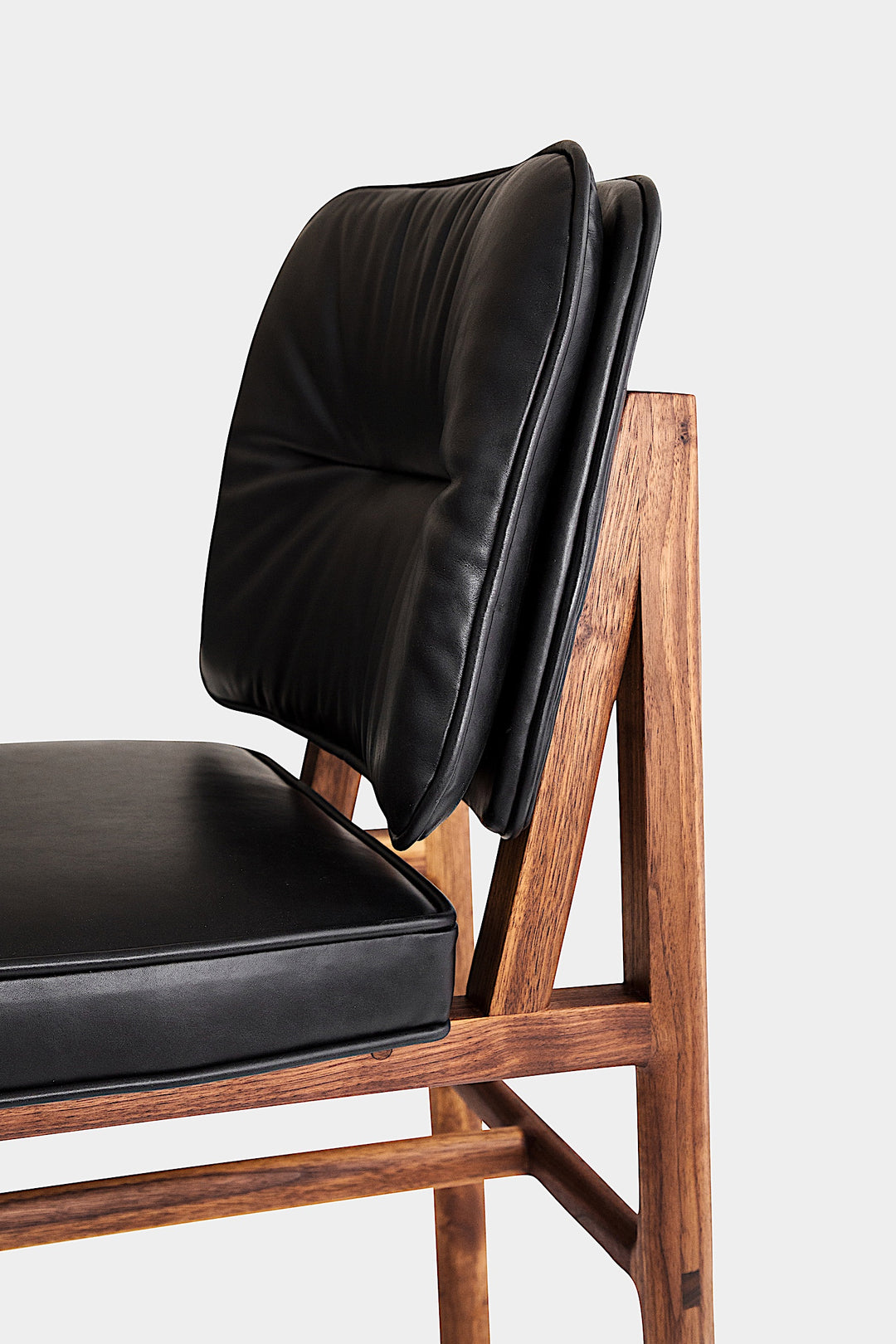 The MORESBY Dining Chair by Earl Home features a custom upholstered black leather seat and backrest, elegantly crafted on a solid wood frame with simple, angular lines.