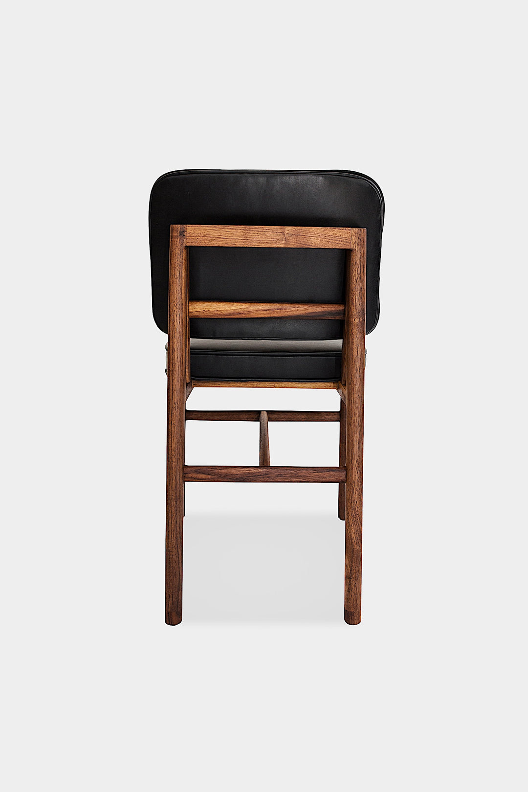 The MORESBY Dining Chair by Earl Home features a custom upholstered black leather seat and backrest, elegantly crafted on a solid wood frame with simple, angular lines.