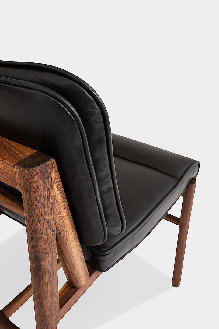 The MORESBY Dining Chair by Earl Home features a custom upholstered black leather seat and backrest, elegantly crafted on a solid wood frame with simple, angular lines.