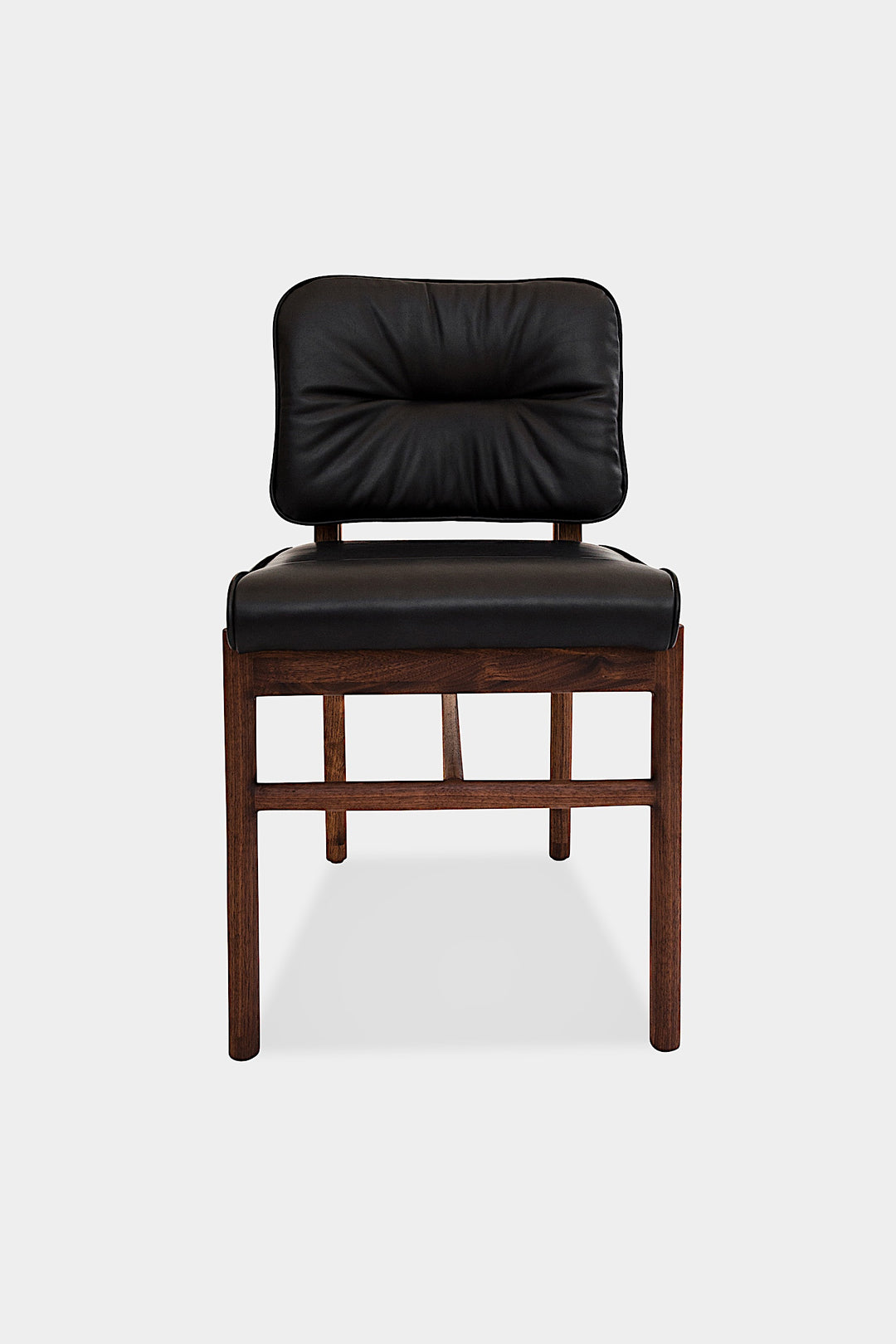 The MORESBY Dining Chair by Earl Home features a custom upholstered black leather seat and backrest, elegantly crafted on a solid wood frame with simple, angular lines.