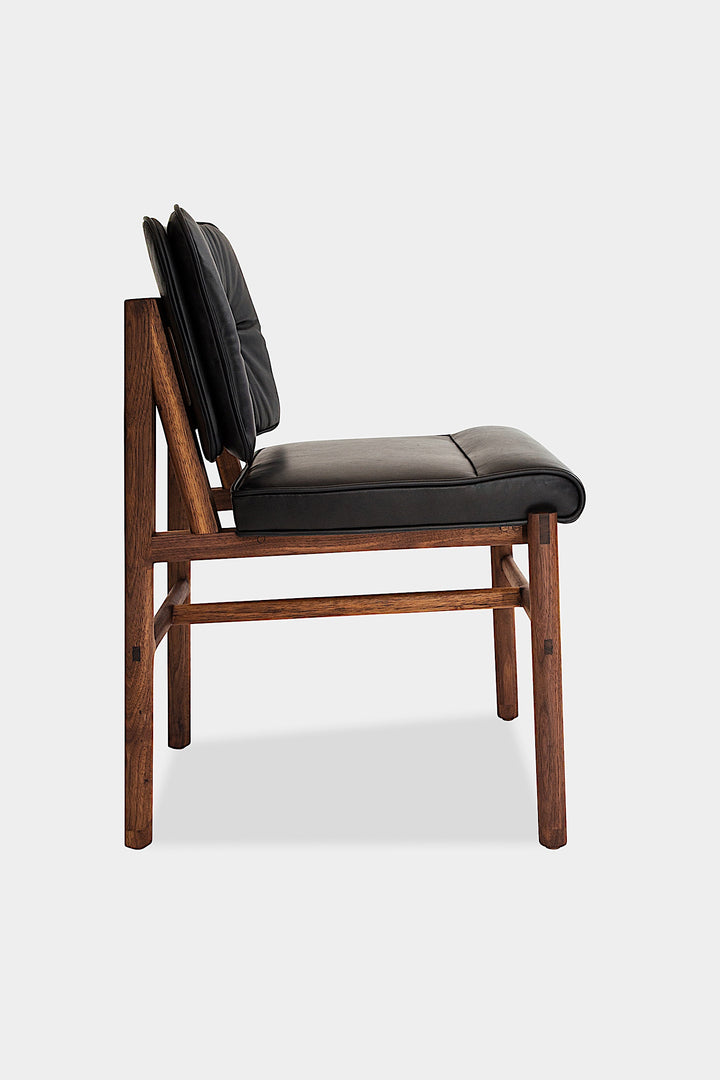 The MORESBY Dining Chair by Earl Home features a custom upholstered black leather seat and backrest, elegantly crafted on a solid wood frame with simple, angular lines.