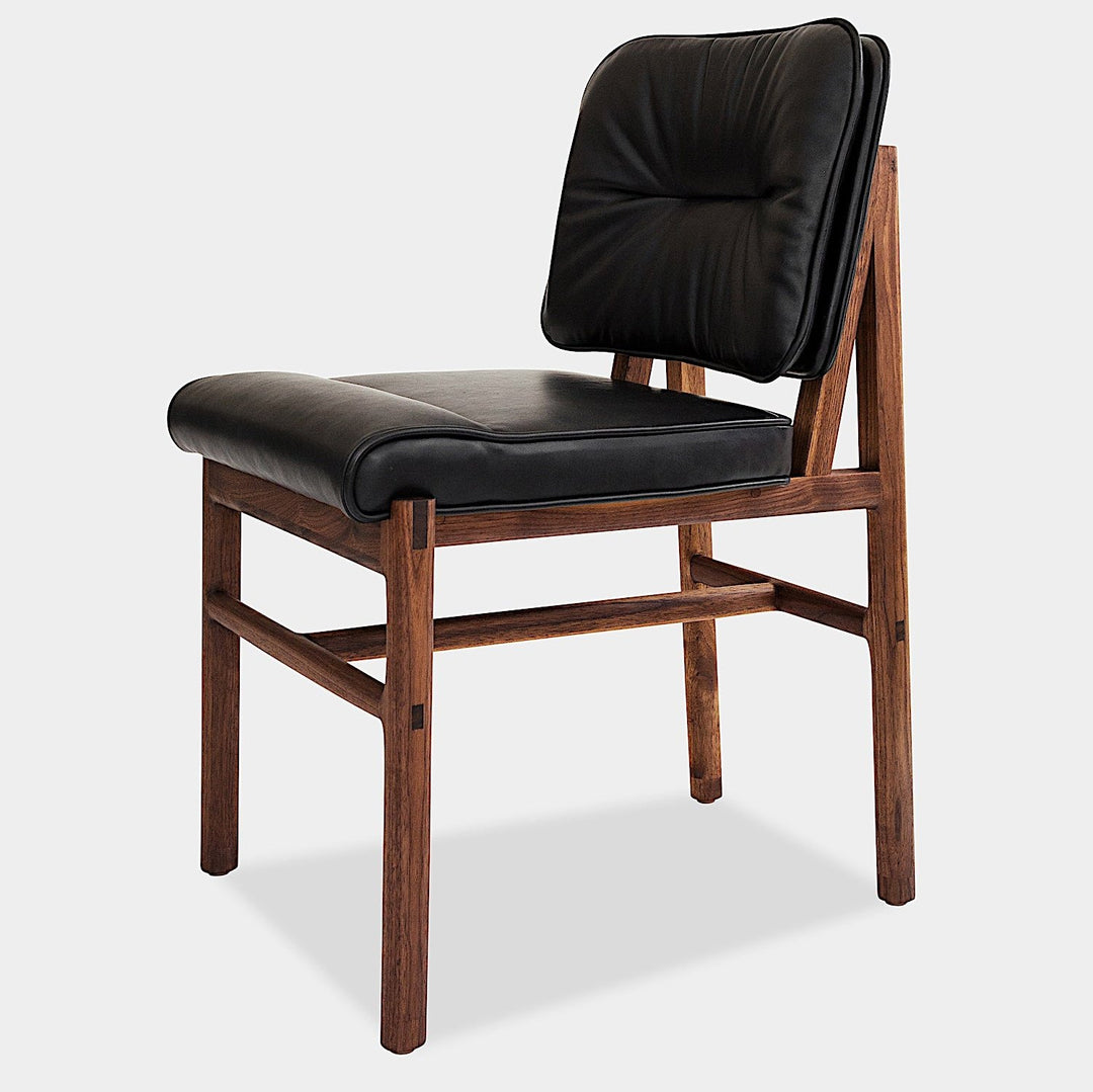 The MORESBY Dining Chair by Earl Home features a custom upholstered black leather seat and backrest, elegantly crafted on a solid wood frame with simple, angular lines.