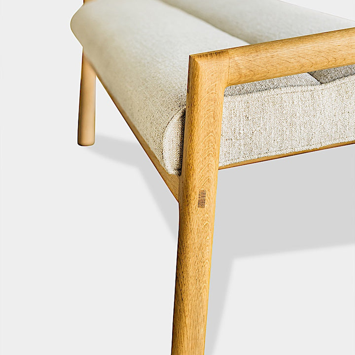 The Earl Home MORESBY Bench highlights a plush light beige cushion on solid wood, featuring clean lines and a minimalist design against a plain background.