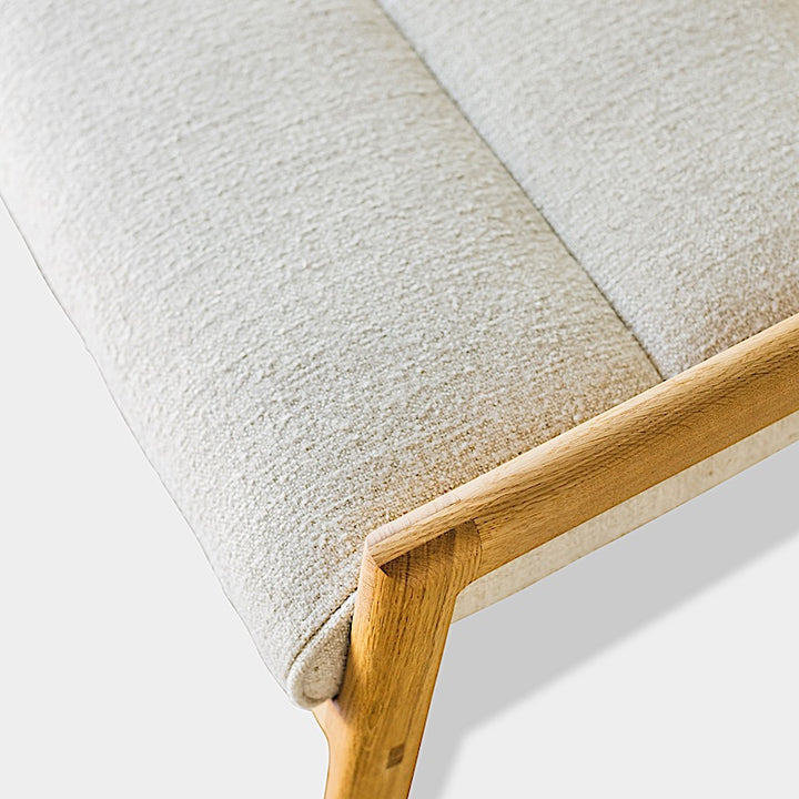 The Earl Home MORESBY Bench highlights a plush light beige cushion on solid wood, featuring clean lines and a minimalist design against a plain background.