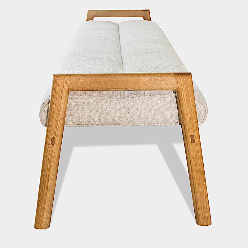 The Earl Home MORESBY Bench highlights a plush light beige cushion on solid wood, featuring clean lines and a minimalist design against a plain background.